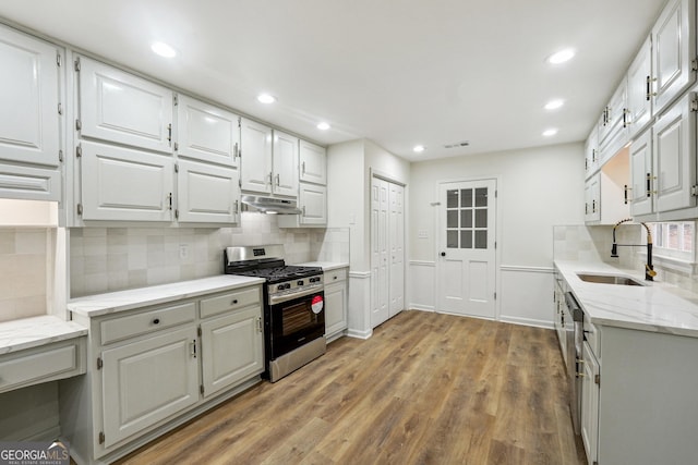 kitchen with sink, gas range, light hardwood / wood-style flooring, decorative backsplash, and white cabinets