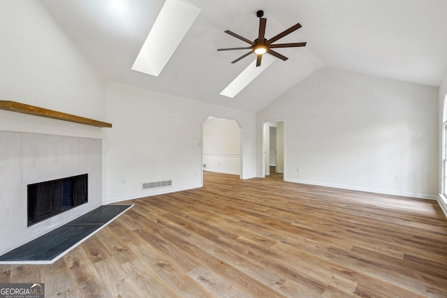 unfurnished living room featuring a skylight, high vaulted ceiling, light hardwood / wood-style flooring, ceiling fan, and a fireplace