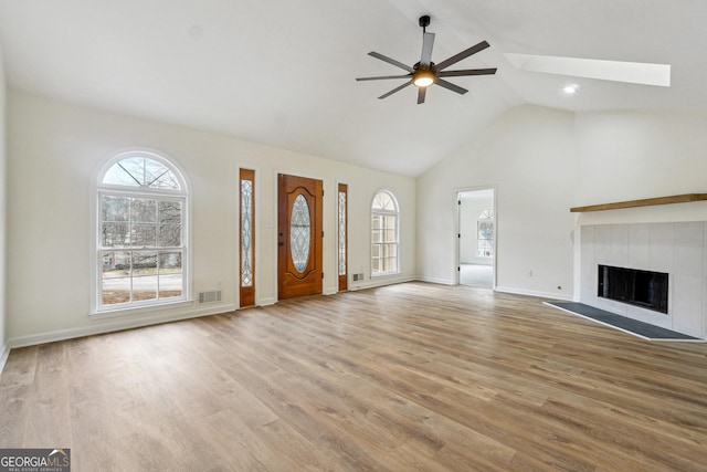 unfurnished living room with ceiling fan, a fireplace, a skylight, and light hardwood / wood-style flooring