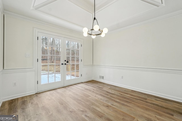 unfurnished dining area featuring hardwood / wood-style floors, a notable chandelier, ornamental molding, and french doors