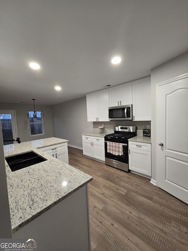 kitchen featuring sink, hanging light fixtures, stainless steel appliances, light stone counters, and white cabinets