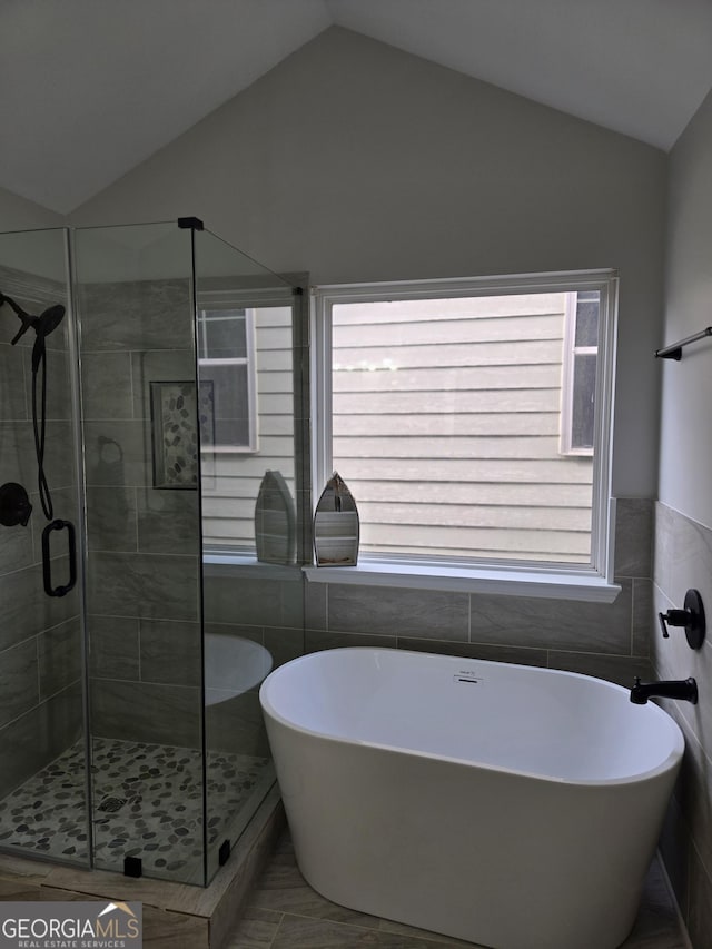 bathroom with independent shower and bath, vaulted ceiling, and tile walls