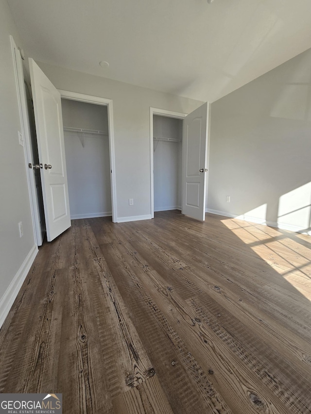 unfurnished bedroom featuring multiple closets and wood-type flooring