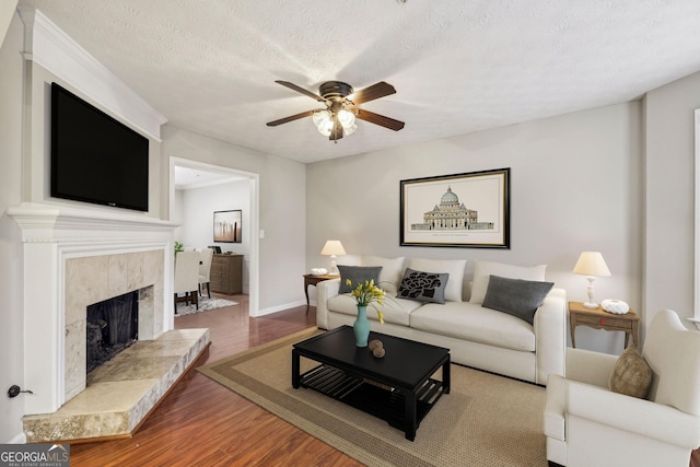 living room featuring ceiling fan, a premium fireplace, hardwood / wood-style floors, and a textured ceiling