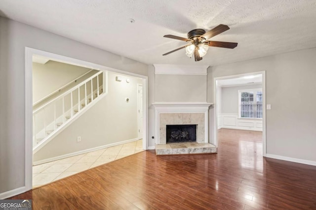 unfurnished living room with a tiled fireplace, wood-type flooring, ceiling fan, and a textured ceiling