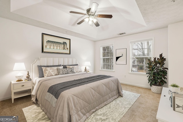 carpeted bedroom with a raised ceiling and ceiling fan