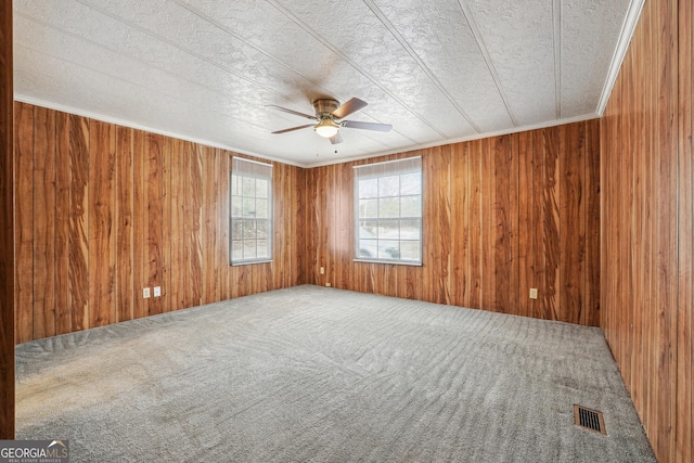 carpeted empty room with ornamental molding, ceiling fan, and wood walls