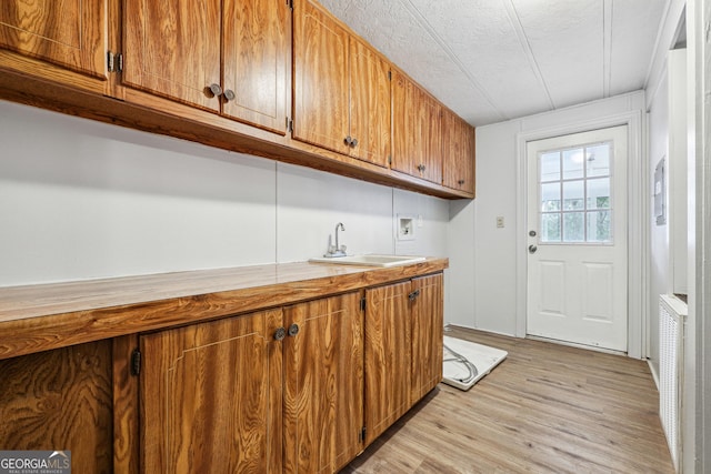 clothes washing area with sink, cabinets, washer hookup, light hardwood / wood-style floors, and a textured ceiling