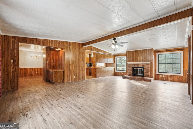 unfurnished living room featuring lofted ceiling, wood walls, a brick fireplace, hardwood / wood-style flooring, and ceiling fan with notable chandelier