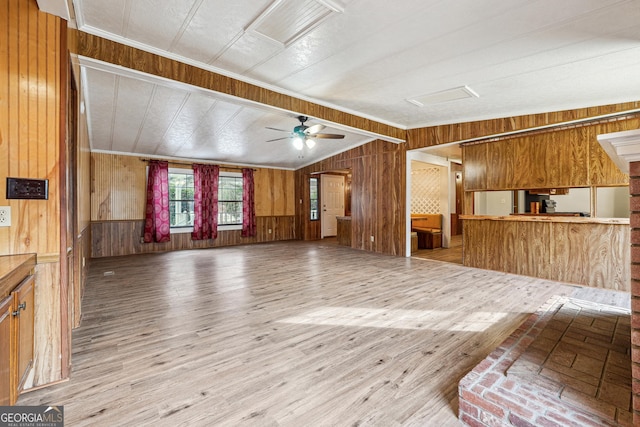 unfurnished living room featuring vaulted ceiling, ceiling fan, light hardwood / wood-style floors, and wood walls