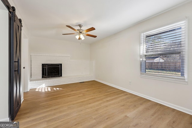 unfurnished living room featuring a fireplace, light hardwood / wood-style floors, a barn door, and ceiling fan