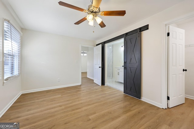 unfurnished bedroom with connected bathroom, a spacious closet, ceiling fan, a barn door, and light hardwood / wood-style floors