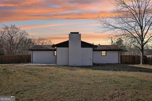 back house at dusk featuring a patio area and a lawn