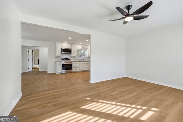 unfurnished living room featuring ceiling fan, sink, and light wood-type flooring