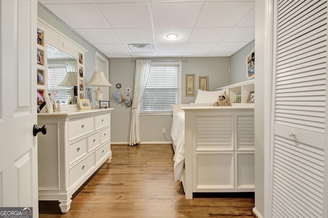 bedroom with multiple windows, a drop ceiling, and light hardwood / wood-style flooring