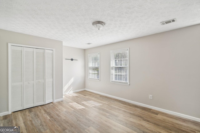 unfurnished bedroom with a textured ceiling, light hardwood / wood-style floors, and a closet