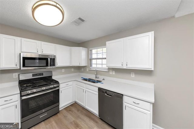 kitchen featuring sink, a textured ceiling, light wood-type flooring, appliances with stainless steel finishes, and white cabinets