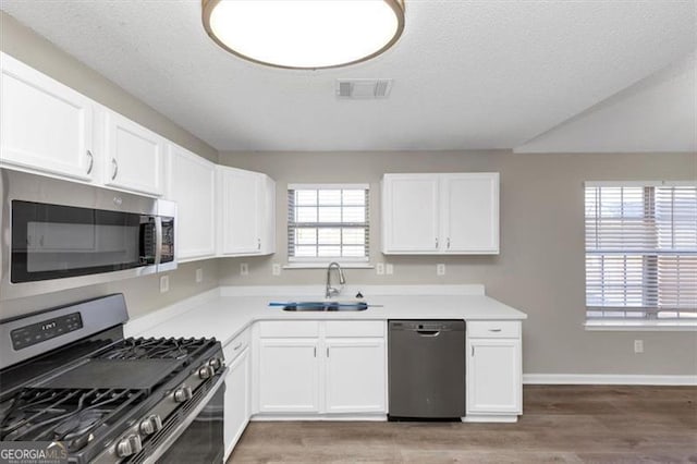 kitchen featuring sink, hardwood / wood-style flooring, white cabinetry, stainless steel appliances, and a textured ceiling