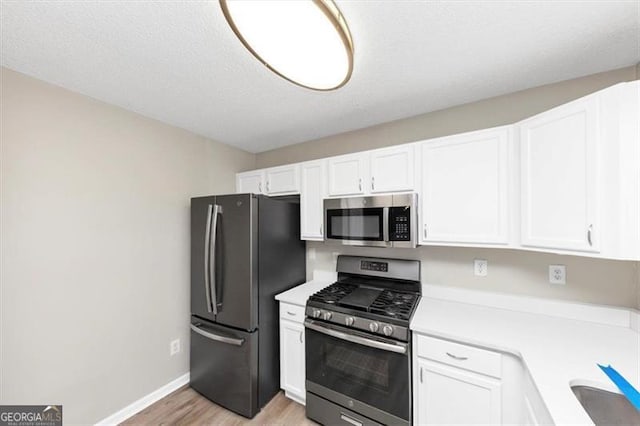 kitchen featuring sink, appliances with stainless steel finishes, light hardwood / wood-style floors, a textured ceiling, and white cabinets