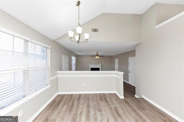 kitchen featuring ceiling fan with notable chandelier, pendant lighting, lofted ceiling, kitchen peninsula, and light wood-type flooring