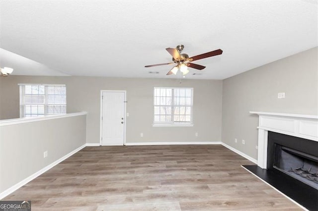 unfurnished living room with ceiling fan with notable chandelier, a wealth of natural light, and light hardwood / wood-style flooring