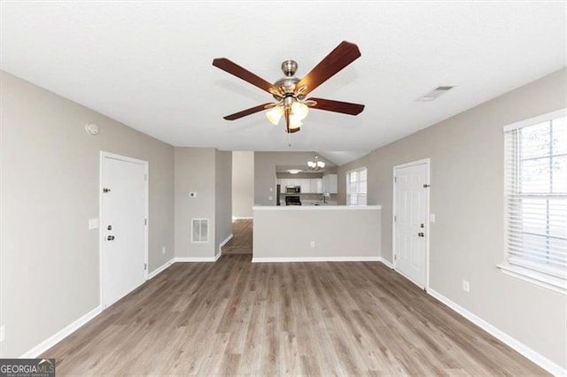 unfurnished living room featuring ceiling fan with notable chandelier and light wood-type flooring