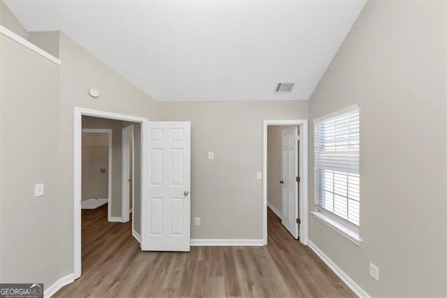 unfurnished bedroom featuring lofted ceiling and light wood-type flooring