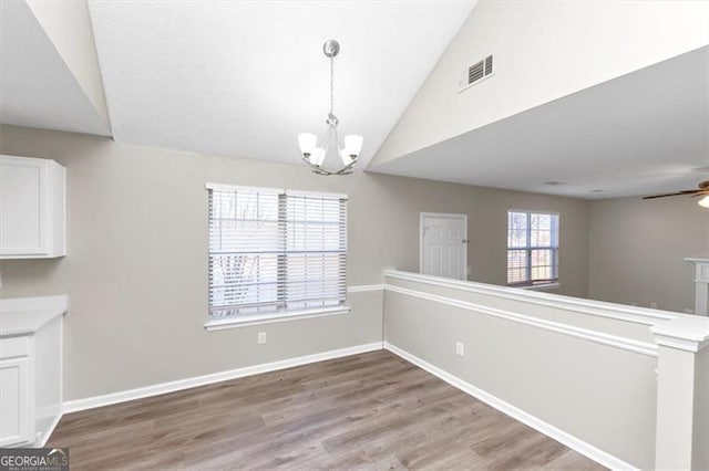 unfurnished dining area featuring vaulted ceiling, ceiling fan with notable chandelier, and light hardwood / wood-style floors