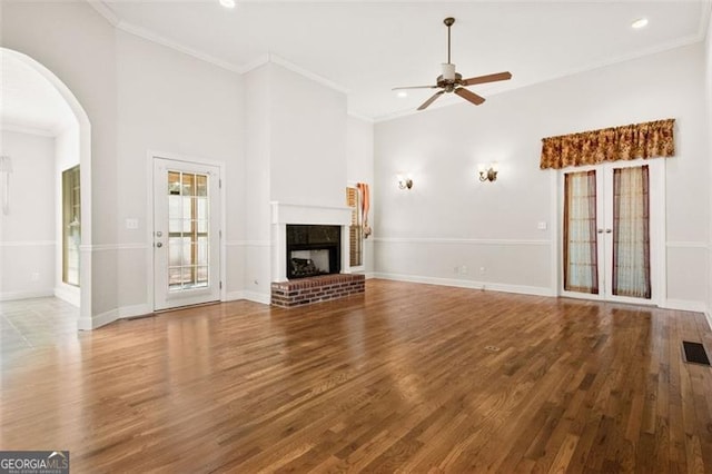 unfurnished living room with wood-type flooring, crown molding, ceiling fan, and a fireplace