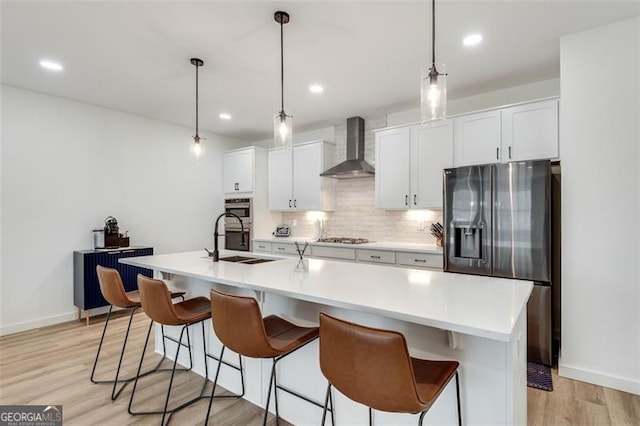 kitchen featuring hanging light fixtures, appliances with stainless steel finishes, a center island with sink, and wall chimney exhaust hood