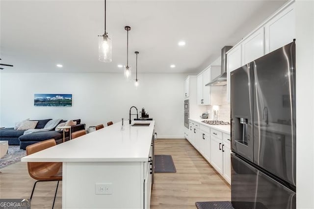 kitchen featuring sink, appliances with stainless steel finishes, hanging light fixtures, white cabinets, and a center island with sink