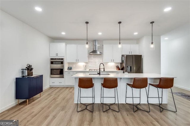 kitchen featuring wall chimney range hood, stainless steel appliances, hanging light fixtures, and a center island with sink