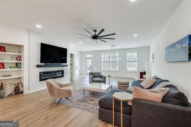 living room with built in shelves, ceiling fan, a fireplace, and light hardwood / wood-style flooring