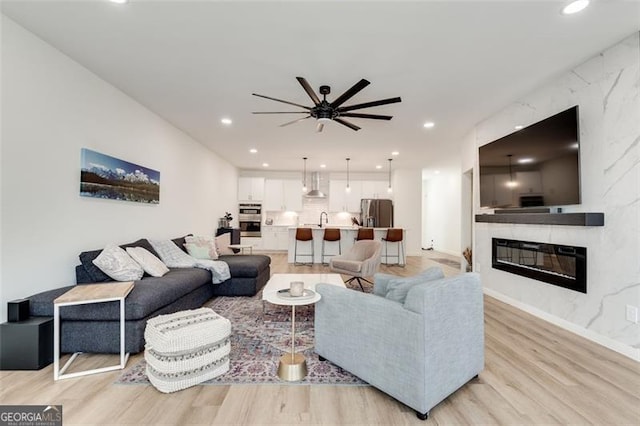 living room with ceiling fan, sink, a fireplace, and light hardwood / wood-style flooring