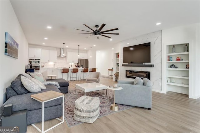 living room with a high end fireplace, light hardwood / wood-style flooring, built in features, and ceiling fan