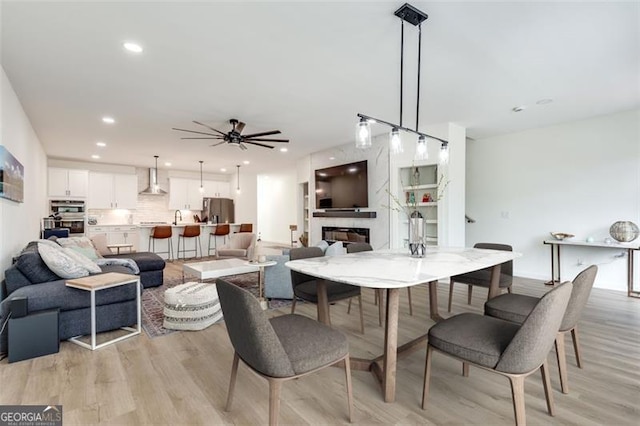 dining area with ceiling fan, sink, a premium fireplace, and light hardwood / wood-style floors