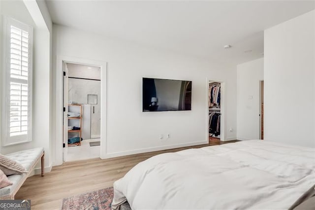 bedroom with a spacious closet, ensuite bath, light hardwood / wood-style floors, and a closet