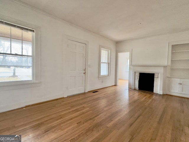 unfurnished living room featuring hardwood / wood-style flooring, crown molding, a brick fireplace, and built in shelves