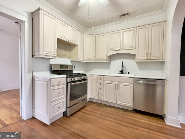 kitchen with appliances with stainless steel finishes, sink, light wood-type flooring, ceiling fan, and a textured ceiling