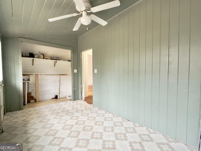 empty room with ceiling fan, lofted ceiling, and wood walls