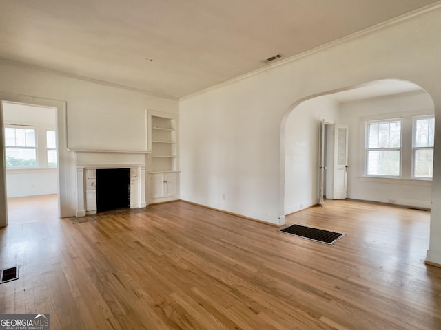 unfurnished living room with crown molding, built in features, and light hardwood / wood-style floors