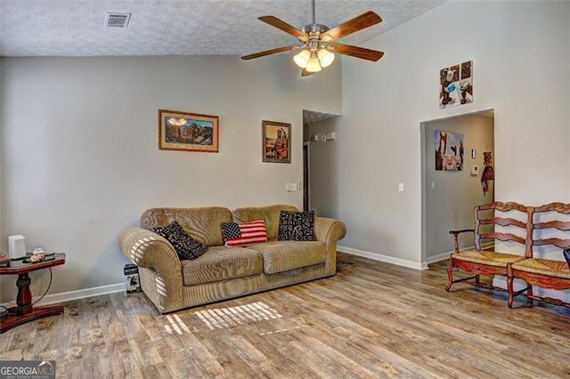 living room featuring ceiling fan, high vaulted ceiling, light hardwood / wood-style flooring, and a textured ceiling