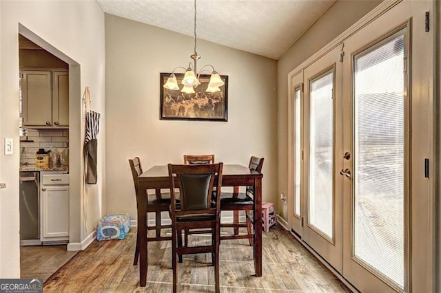 dining room with lofted ceiling, light hardwood / wood-style flooring, a notable chandelier, a textured ceiling, and french doors