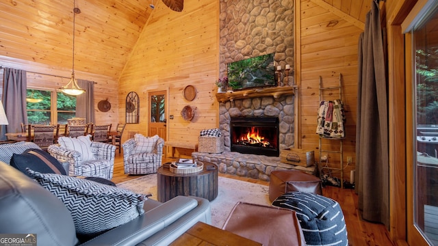 living room featuring hardwood / wood-style flooring, wooden walls, high vaulted ceiling, and a stone fireplace