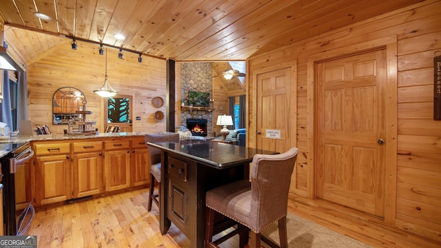 kitchen featuring a kitchen bar, decorative light fixtures, dark stone countertops, wooden ceiling, and wooden walls