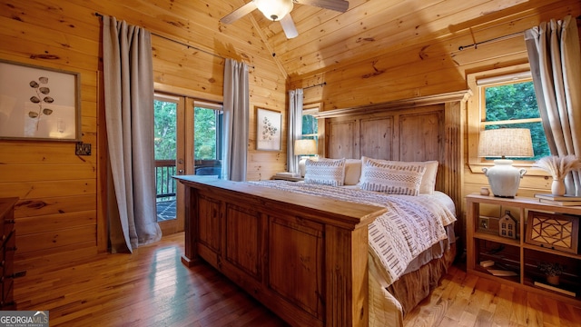 bedroom featuring multiple windows, access to exterior, vaulted ceiling, and wood walls