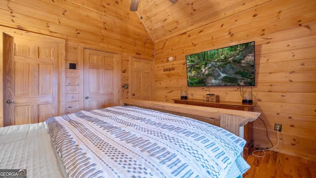 bedroom featuring hardwood / wood-style flooring, wooden walls, and vaulted ceiling