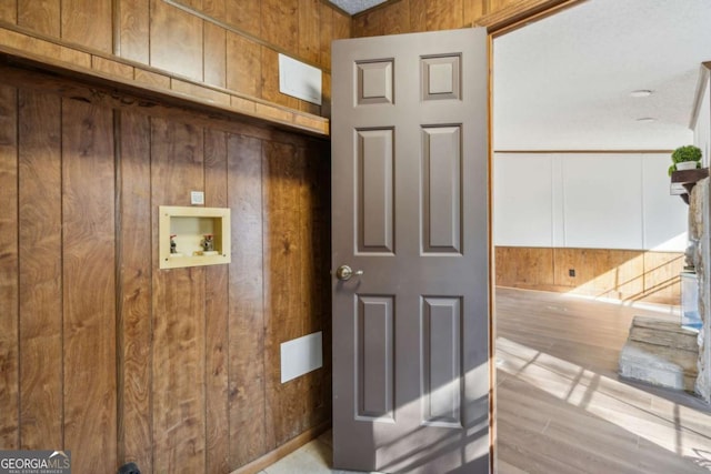 interior space with light hardwood / wood-style floors, hookup for a washing machine, and wood walls