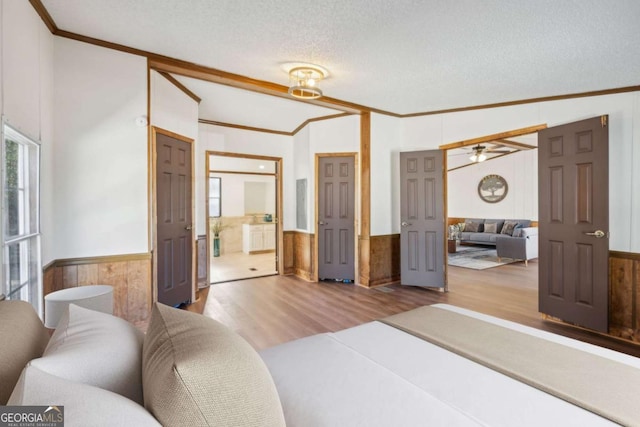 bedroom featuring lofted ceiling, light hardwood / wood-style flooring, ornamental molding, and a textured ceiling