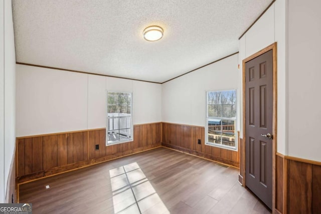 spare room featuring hardwood / wood-style flooring, a healthy amount of sunlight, wooden walls, and a textured ceiling